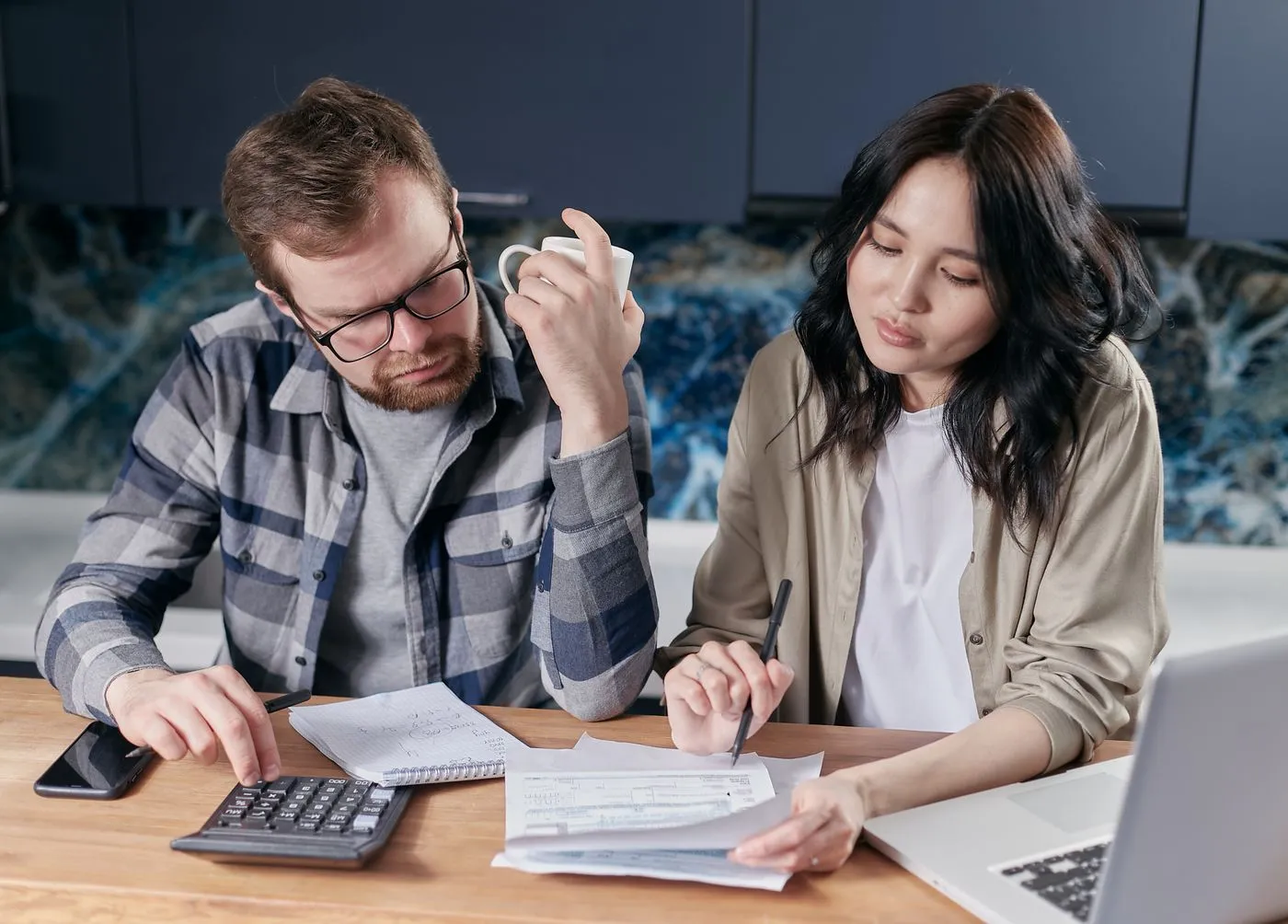 A couple at a kitchen table going through paperwork with a laptop and calculator